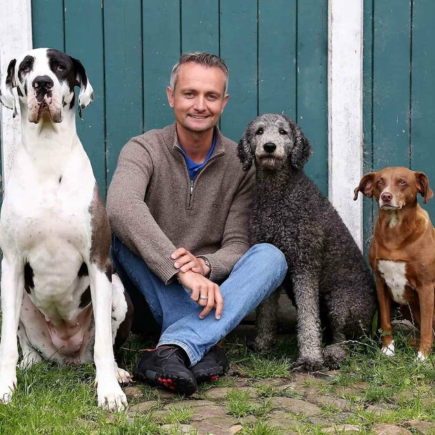 Marc Eichstedt sitzt vor einem grünem Scheunentor mit drei Hunden