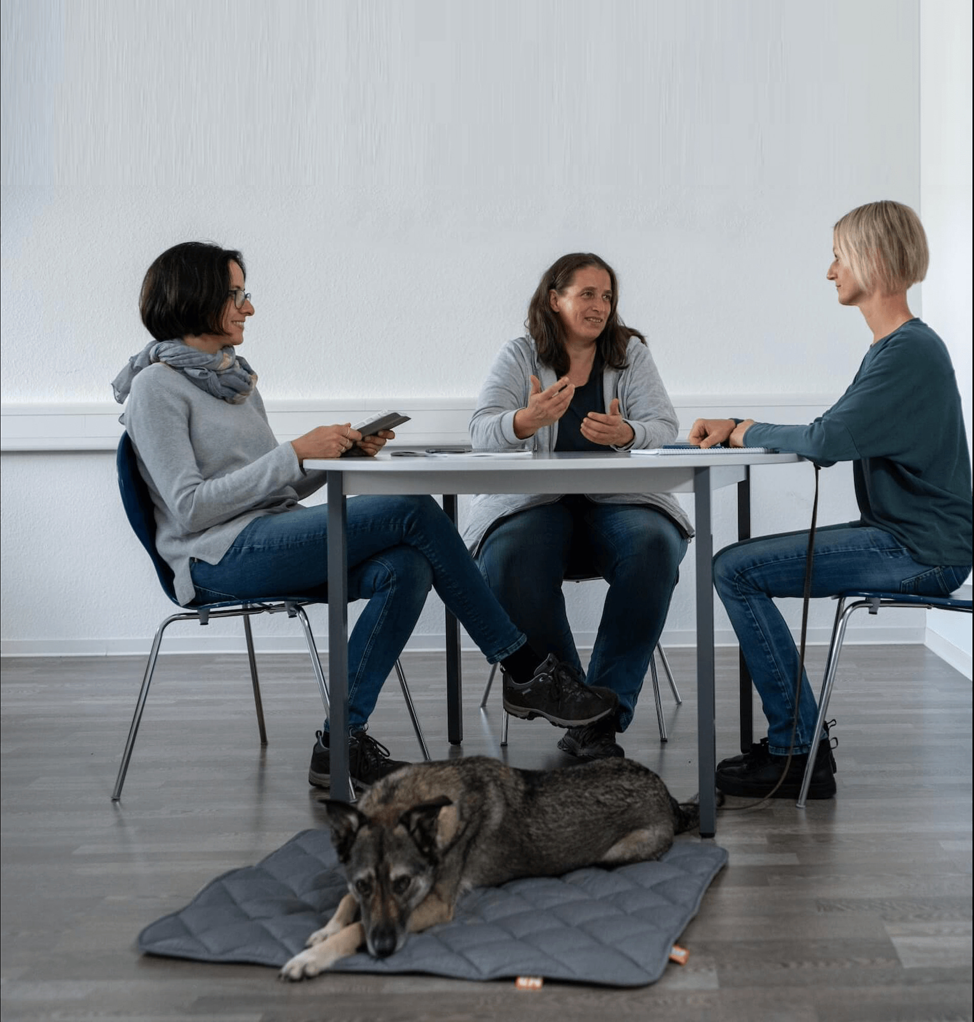 Drei Frauen sitzen an einem Tisch, wo ein Hund drunter liegt