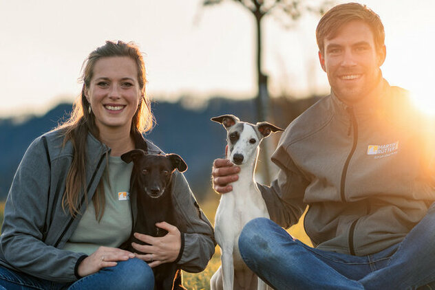 Ein Hund mit weißen Fell sitzt zwischen einer Frau und einem Mann