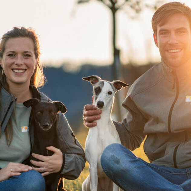 Ein Hund mit weißen Fell sitzt zwischen einer Frau und einem Mann