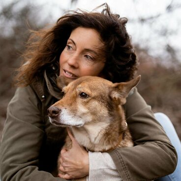 Frau mit dunklen Haaren umarmt sitzenden Hund