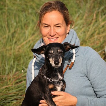 Frau mit hellgrauem Pullover hat einen Hund auf ihrem Schoß sitzen