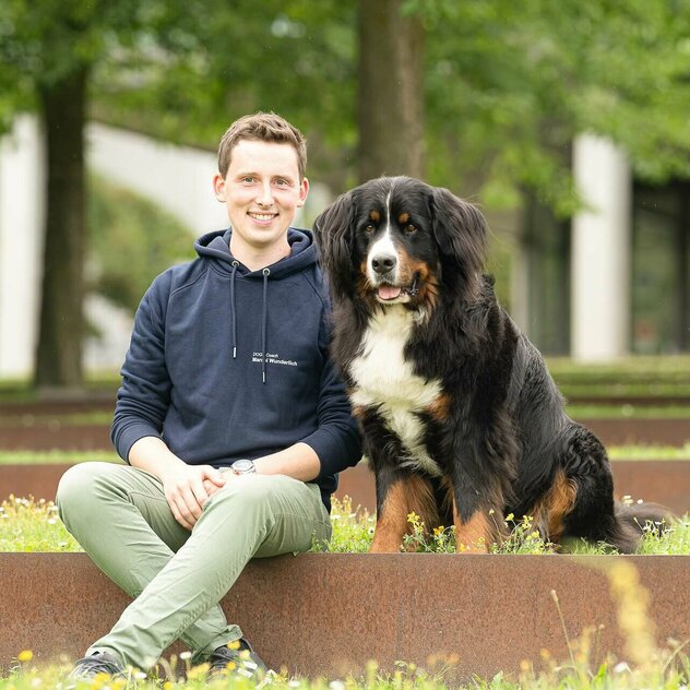 Mann sitzt neben Hund mit schwarzem Fell