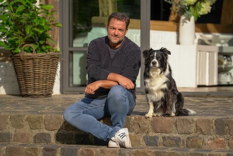 Martin Rütter sitzt mit seinem Hund Emma auf einer Treppenstufe