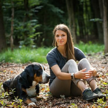 Frau und Hund mit schwarzem Fell sitzen im Wald