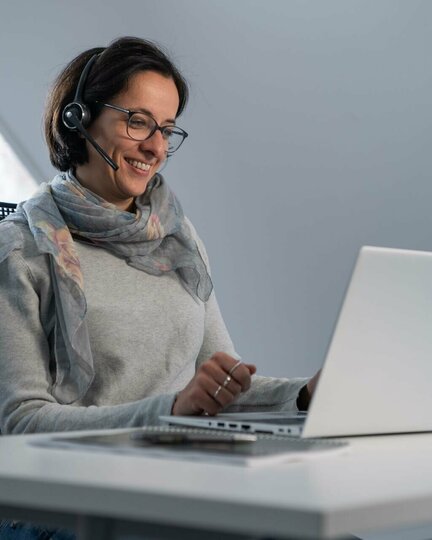 Frau mit Headset, die am Schreibtisch vor ihrem Laptop sitzt