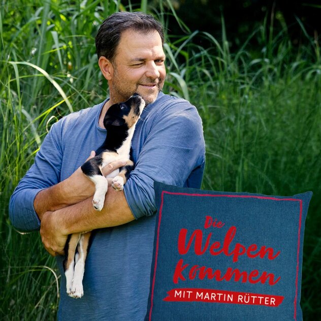 Martin Rütter hält Welpen auf dem Arm. Logo der TV-Show "Die Welpen kommen" unten rechts.