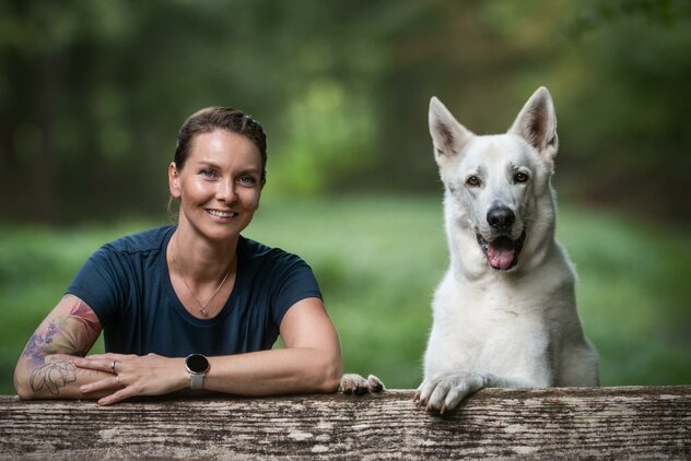 Frau und Hund mit weißem Fell lehnen sich an einen Baum