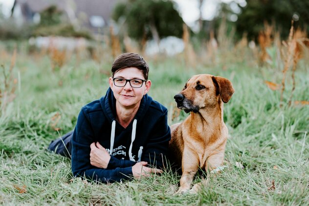 Mann und Hund mit hellem Fell liegen im Gras 