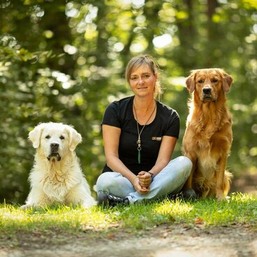 Frau sitzt zwischen zwei Hunden in der Natur