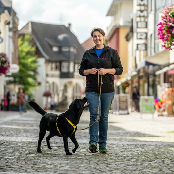 Alicia geht mit ihrem schwarzen Labrador Mando auf einer Kopfsteinpflasterstraße spazieren