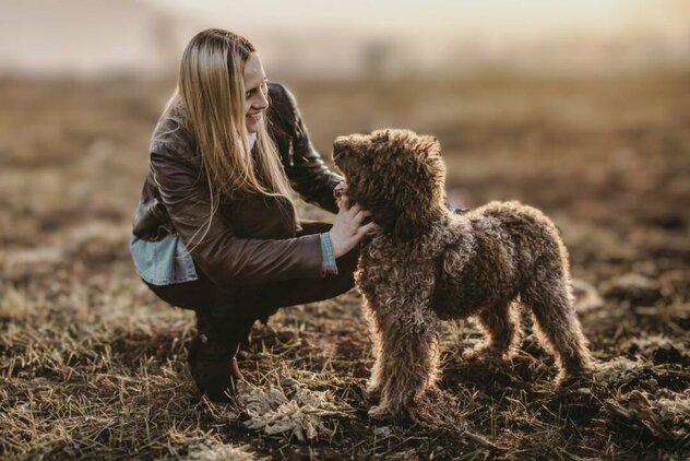blonde Frau kniet neben Hund beide scheuen sich vertrauensvoll an