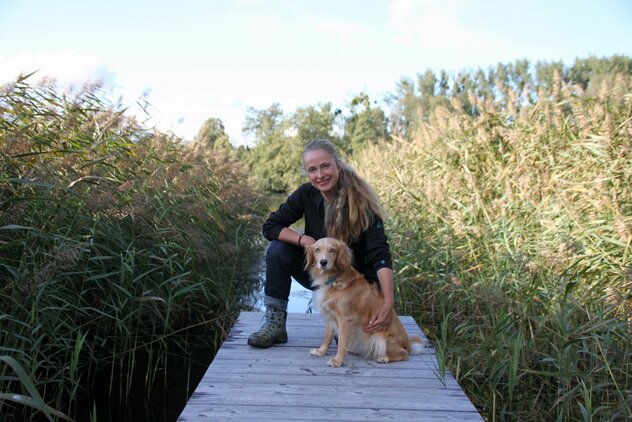 Conny mit ihrem Hund Elsa auf einem Steg am Wasser