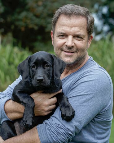 Martin Rütter mit schwarzem Labradorwelpen auf dem Arm.