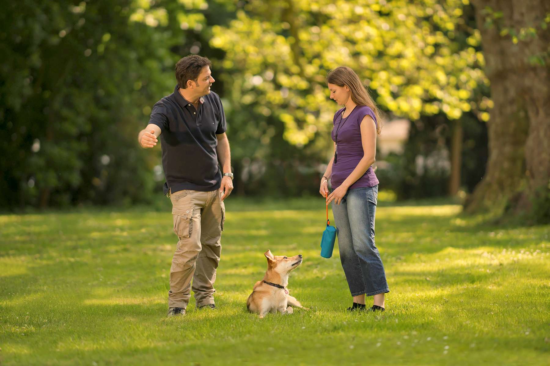 Martin Rütter im Gespräch mit Kunden, während Hund im Platz liegt und zu Frauchen und Futterbeutel schaut.